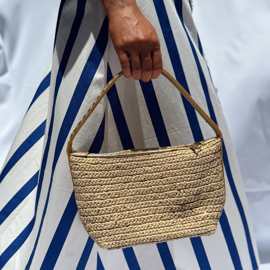 Person holding a woven handbag with a blue and white striped dress in the background